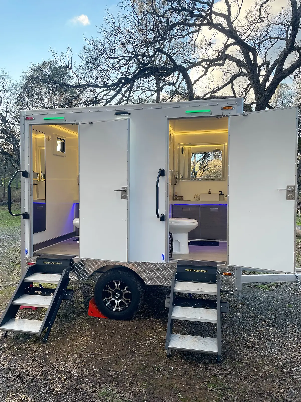 Two-stall restroom trailer with lit interiors at dusk
